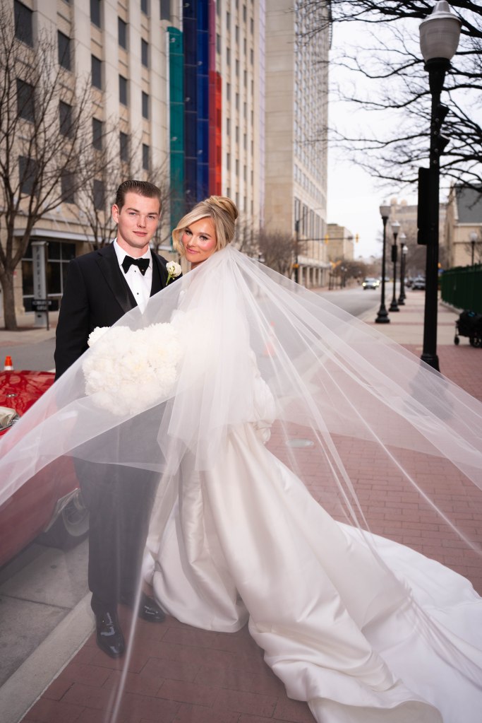 Newlyweds outside St. Patrick’s Cathedral posing next to their red getaway car

