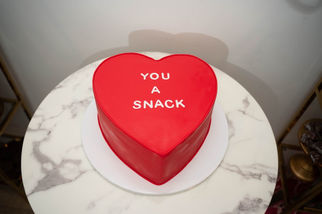 Heart-shaped red groom’s cake with “You a snack” written on it
