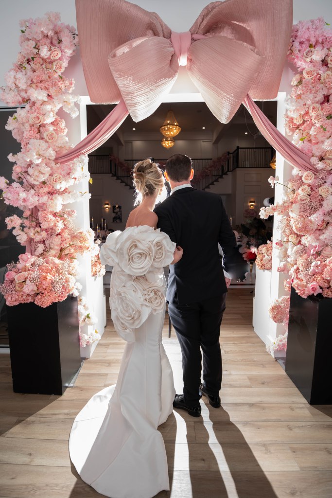 Bride and groom walking into reception under a massive pink bow installation
