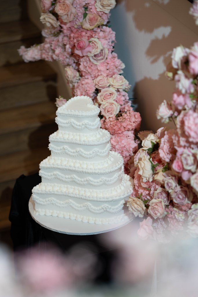 All-white heart-shaped wedding cake surrounded by pink floral arrangements
