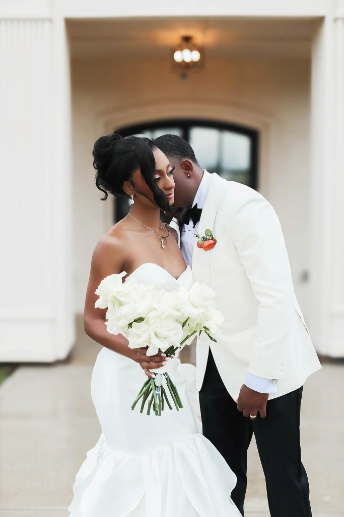 Bride and groom sharing an intimate moment indoors after their wedding ceremony while holding a white floral bouquet.