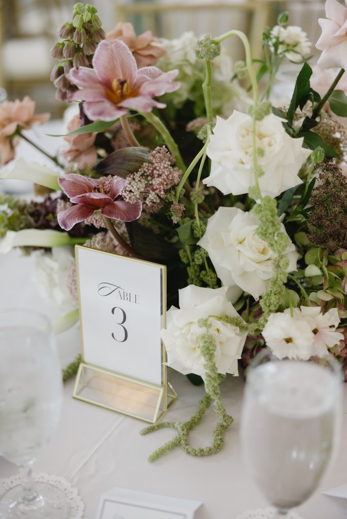 Elegant wedding reception table setting featuring lush green, white, and pink floral arrangements with romantic candlelight, layered place settings, and timeless wedding decor details.