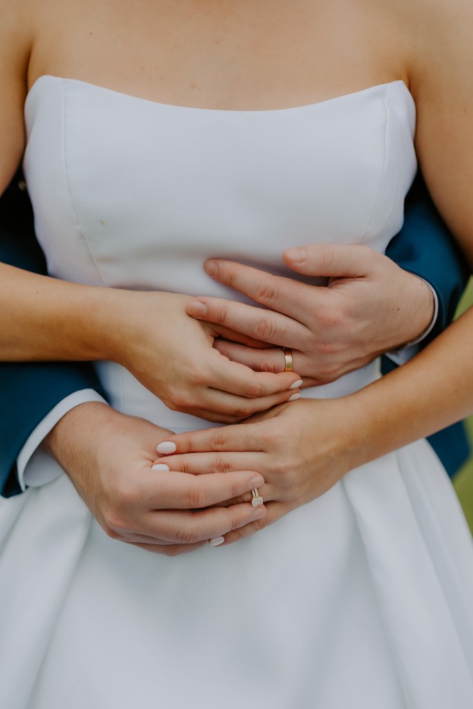Close-up bridal portrait featuring a bride in a strapless wedding dress with hands gently placed around her waist showing elegant wedding details.